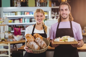 Portrait of waiter and waitress holding a tray of bread and meal in cafe