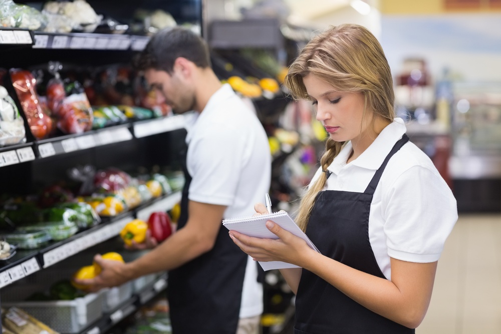 Serious staff woman writing on notepad at supermarket