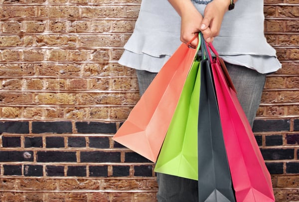 girl in bright colours holding shopping bags over a brick wall