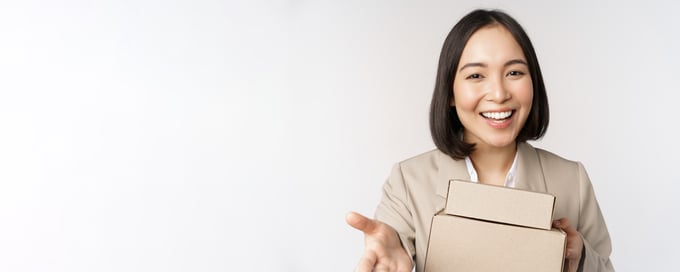 portrait-of-business-woman-asian-saleswoman-pointing-at-you-giving-boxes-with-orders-standing-in-suit-over-white-background